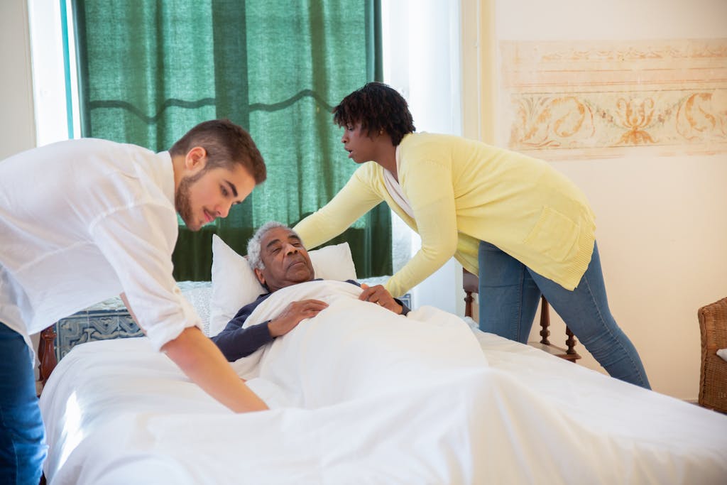 Home Caregivers supporting an elderly man lying in bed, providing assistance and comfort.