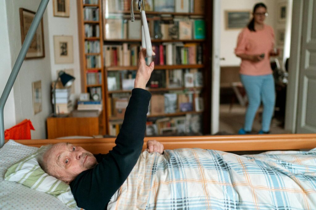 Holistic Care Senior man in bed with caregiver in Prague home, surrounded by books.