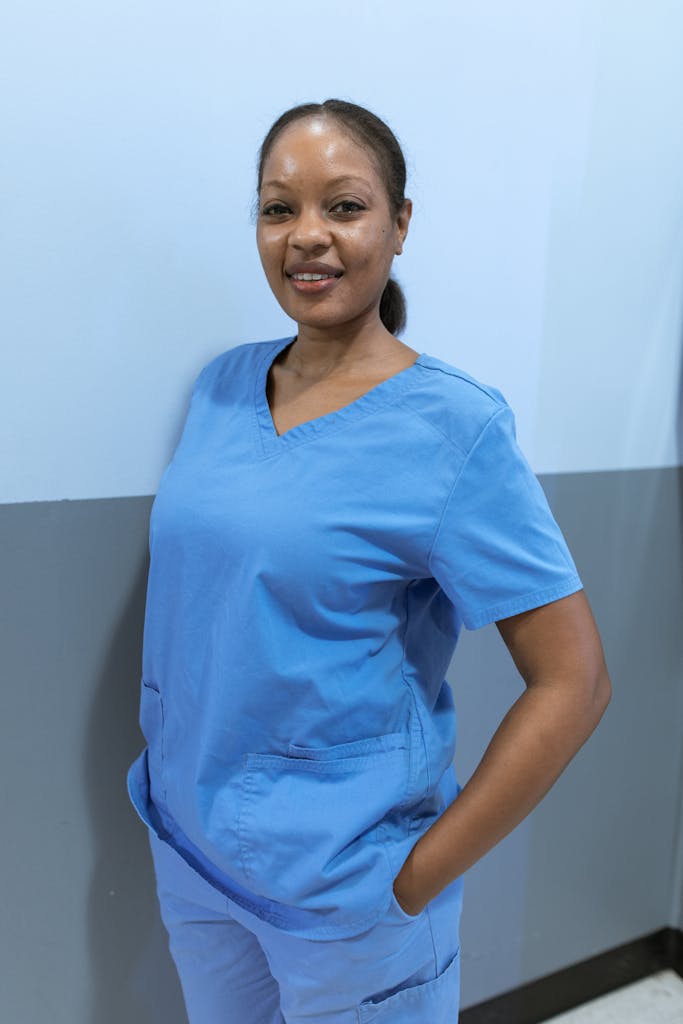 About Us African American nurse smiling confidently indoors, wearing blue scrubs.