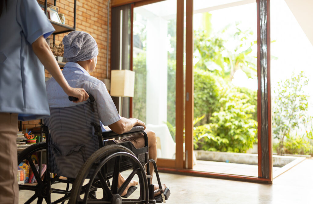 Care Services old asian male with cancer wear sitting on wheelchair, she feeling lonely and depress, she look at window and hope to see family, elderly healthcare.